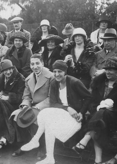 René Lacoste, Suzanne Lenglen, and their respective mothers seated in the stands of a tennis court on the Côte d’Azur
