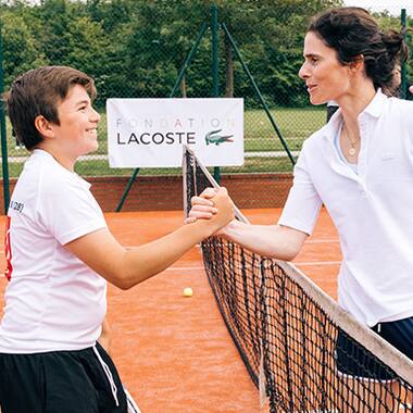 Boy and tennis trainer sharing a high five on a Lacoste Foundation tennis court