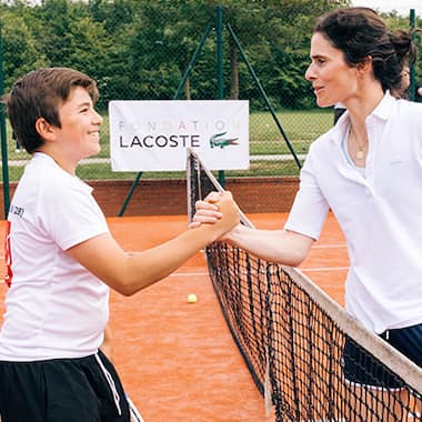 Ragazzo e allenatore di tennis che si danno il cinque su un campo da tennis della Fondazione Lacoste
